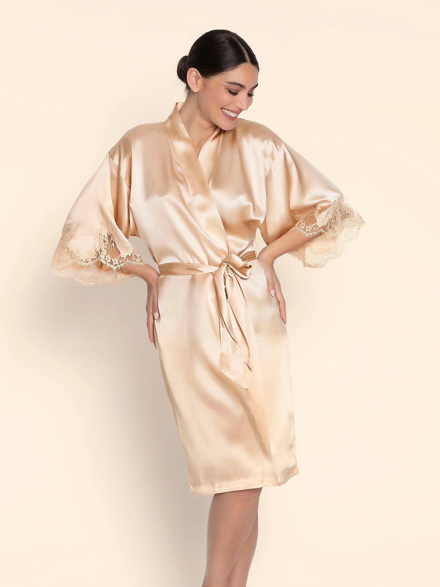 Woman wearing a beige satin robe with lace trim on a plain background