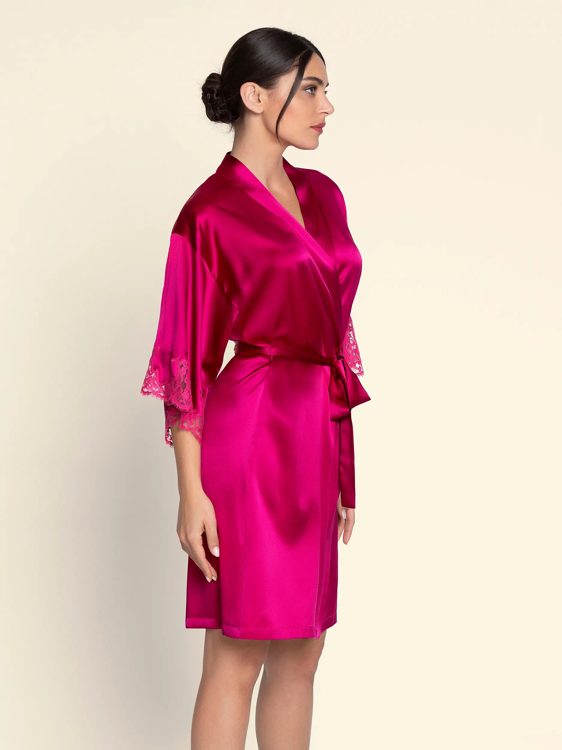 Woman wearing a bright pink satin robe on a beige background